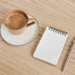 Notebook, pen and coffee on a wooden desk, representing AI proposal writers for freelancers and agencies
