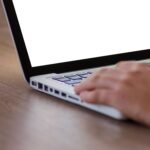 Hand using a laptop with a blank screen, representing choosing between ChatGPT, Claude, and Gemini for small business